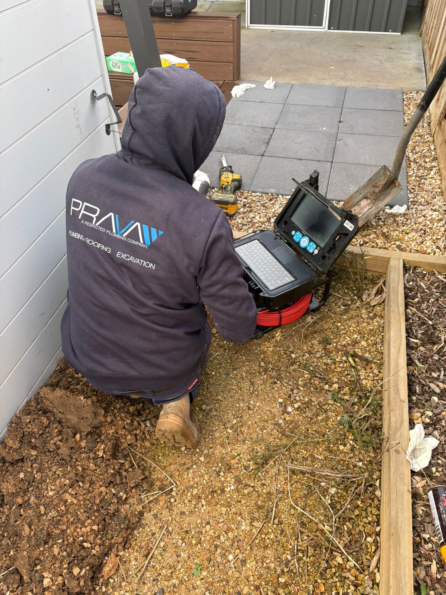 Prava technician running a CCTV drain camera beside a house