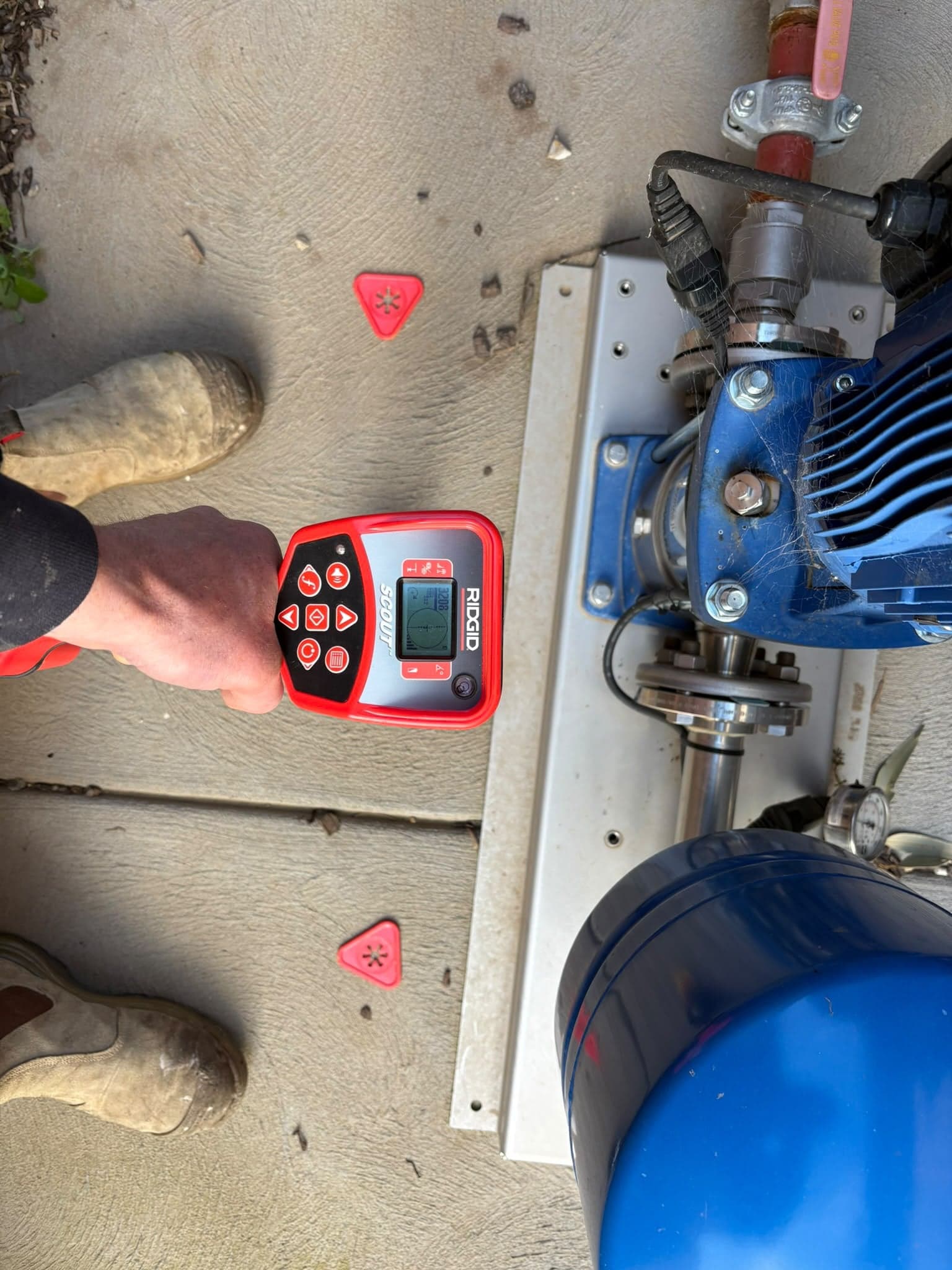 Prava plumber using an electronic locator to trace a drain line beside a pump