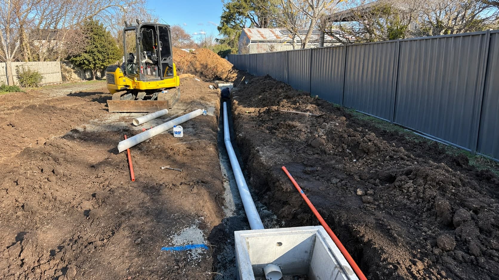 New stormwater drainage line and concrete pit laid in a trench beside a fence