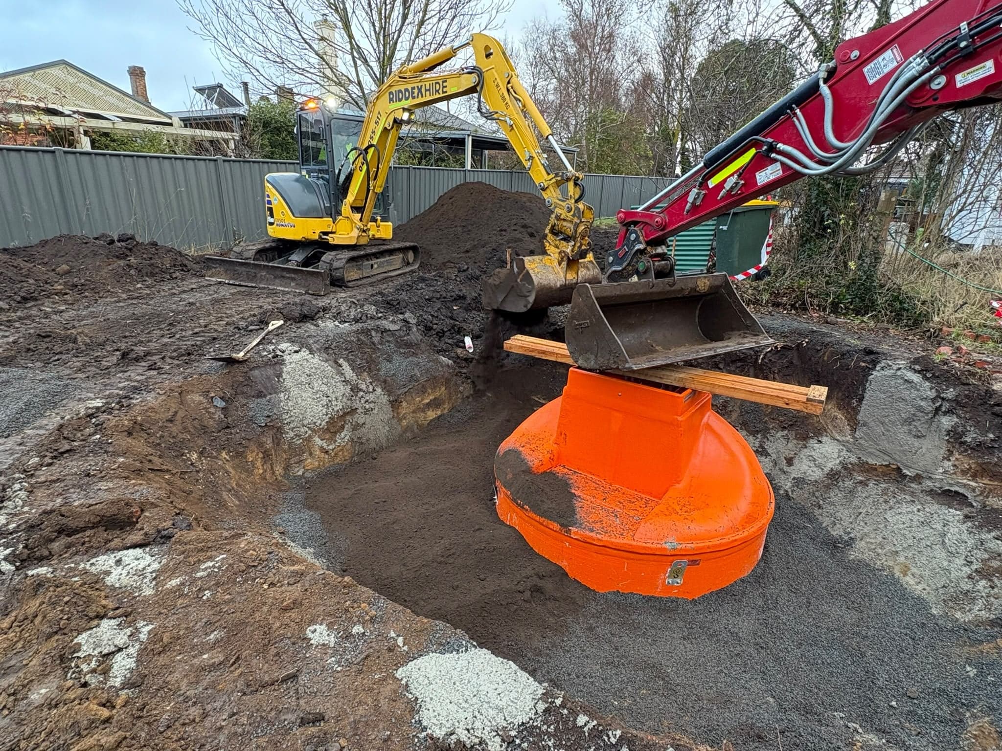 Excavators lowering a new orange stormwater pit into an excavation