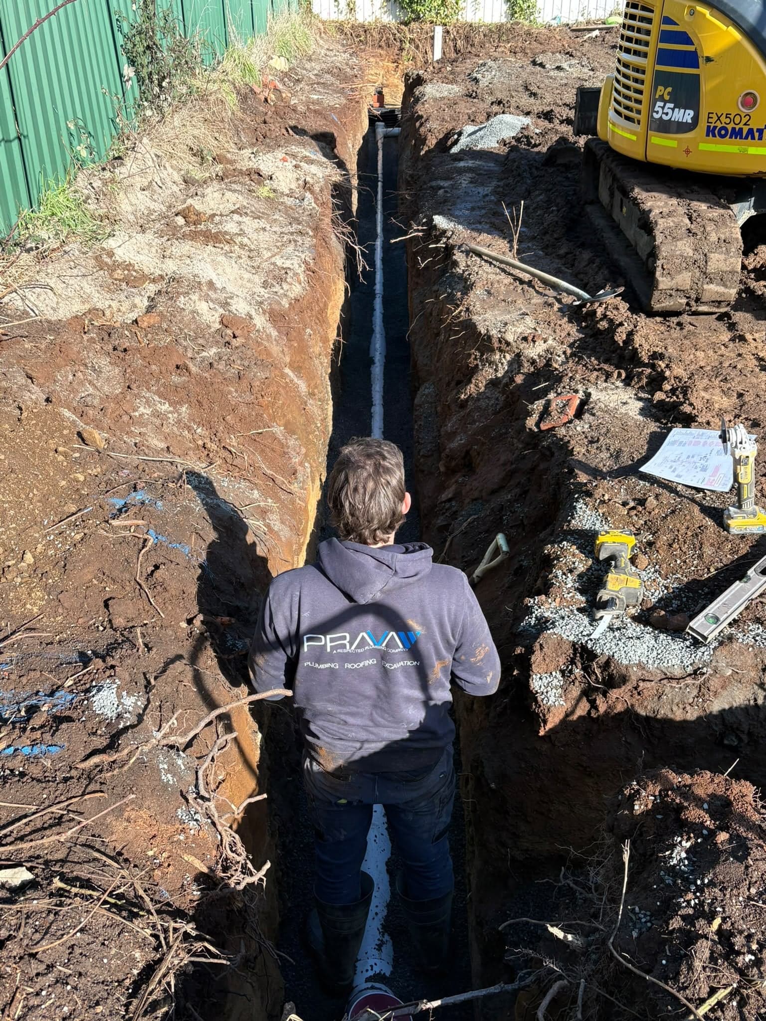 Prava plumber laying a drainage pipe in a deep trench