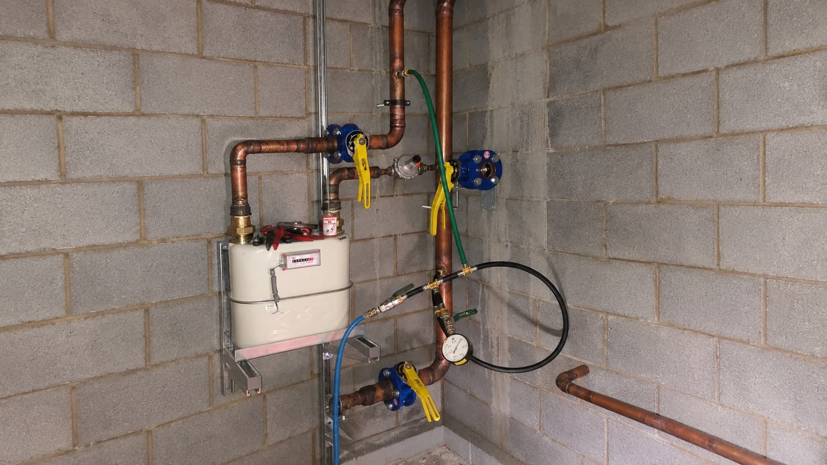 Gas meter, copper gas pipework, isolation valves and a pressure test gauge in a meter room