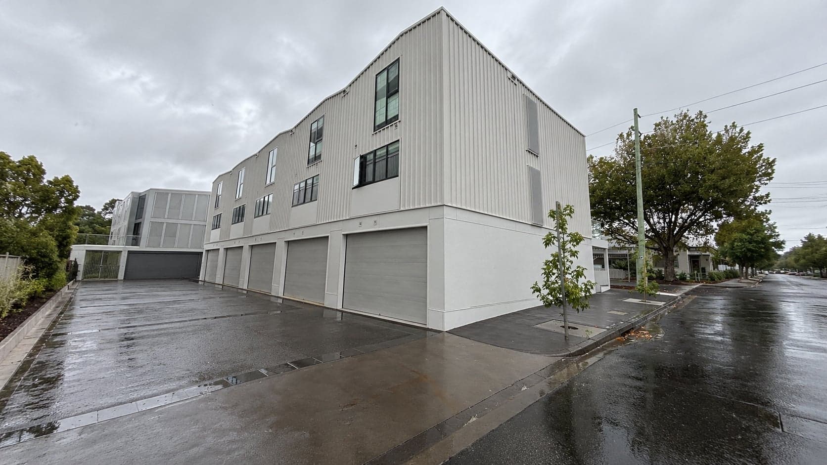 Townhouse building with roller doors on a wet street, a completed Prava project