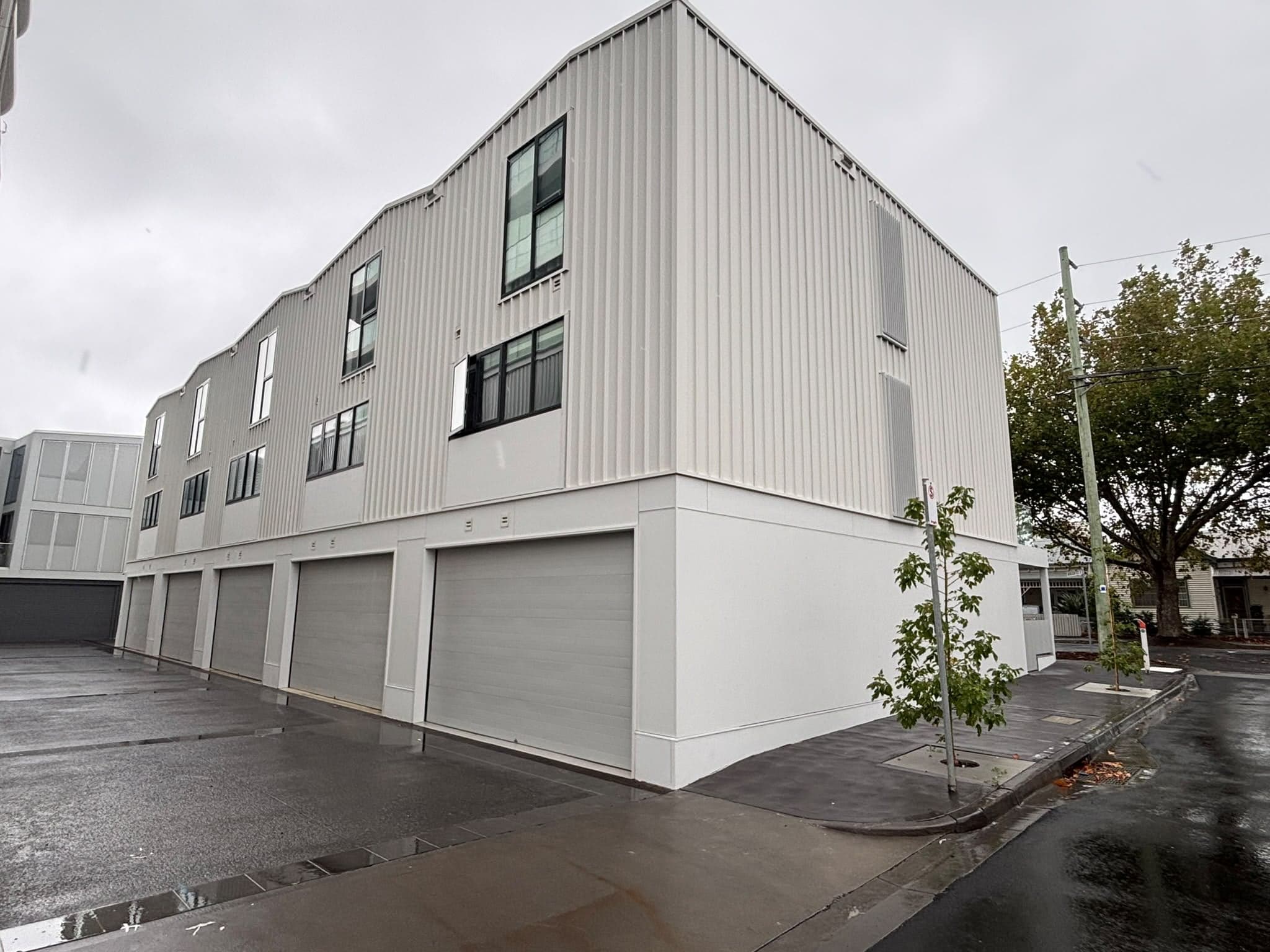 Townhouse building with roller doors on a wet street, a completed Prava project