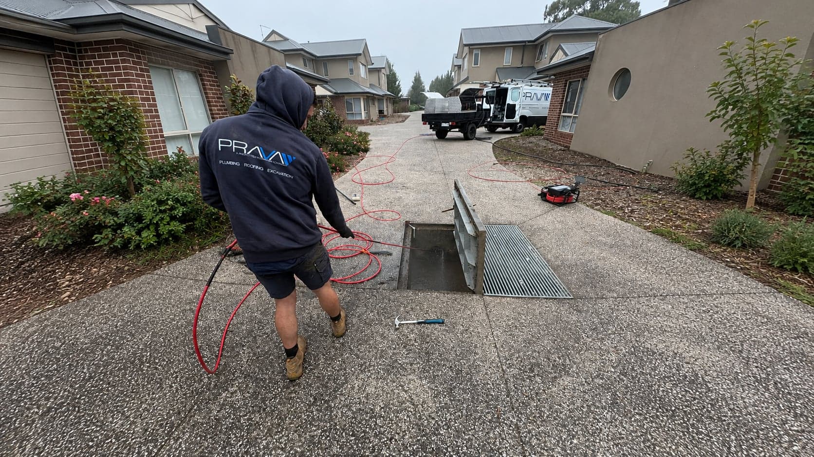 Prava technician clearing a stormwater pit at a townhouse complex, with the service van behind