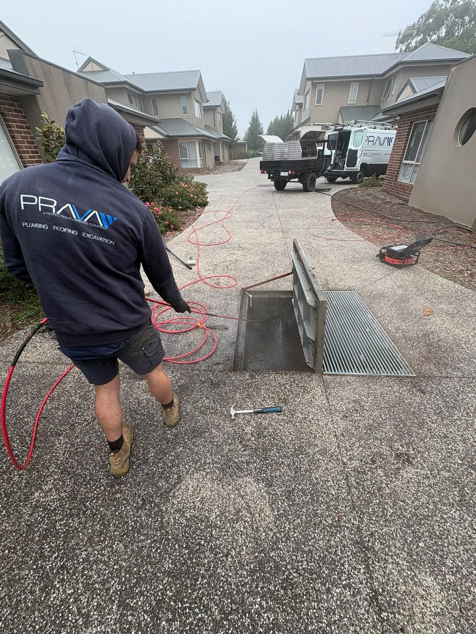 Prava technician clearing a stormwater pit at a townhouse complex, with the service van behind