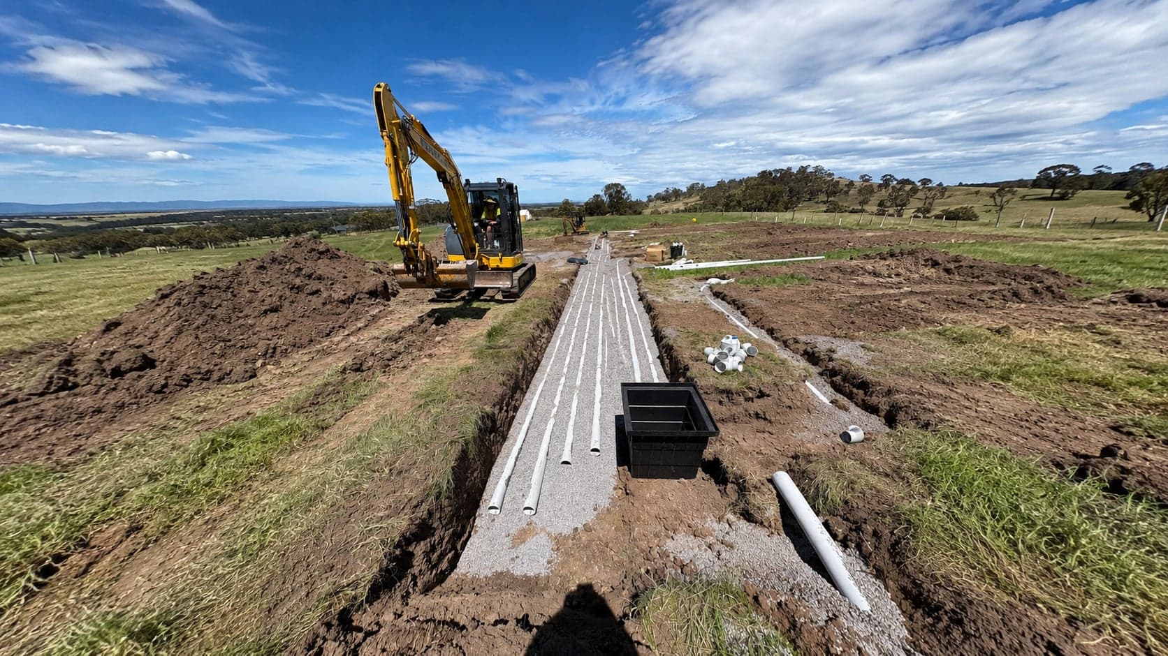 Prava excavator laying new drainage pipes in a trench on a rural site