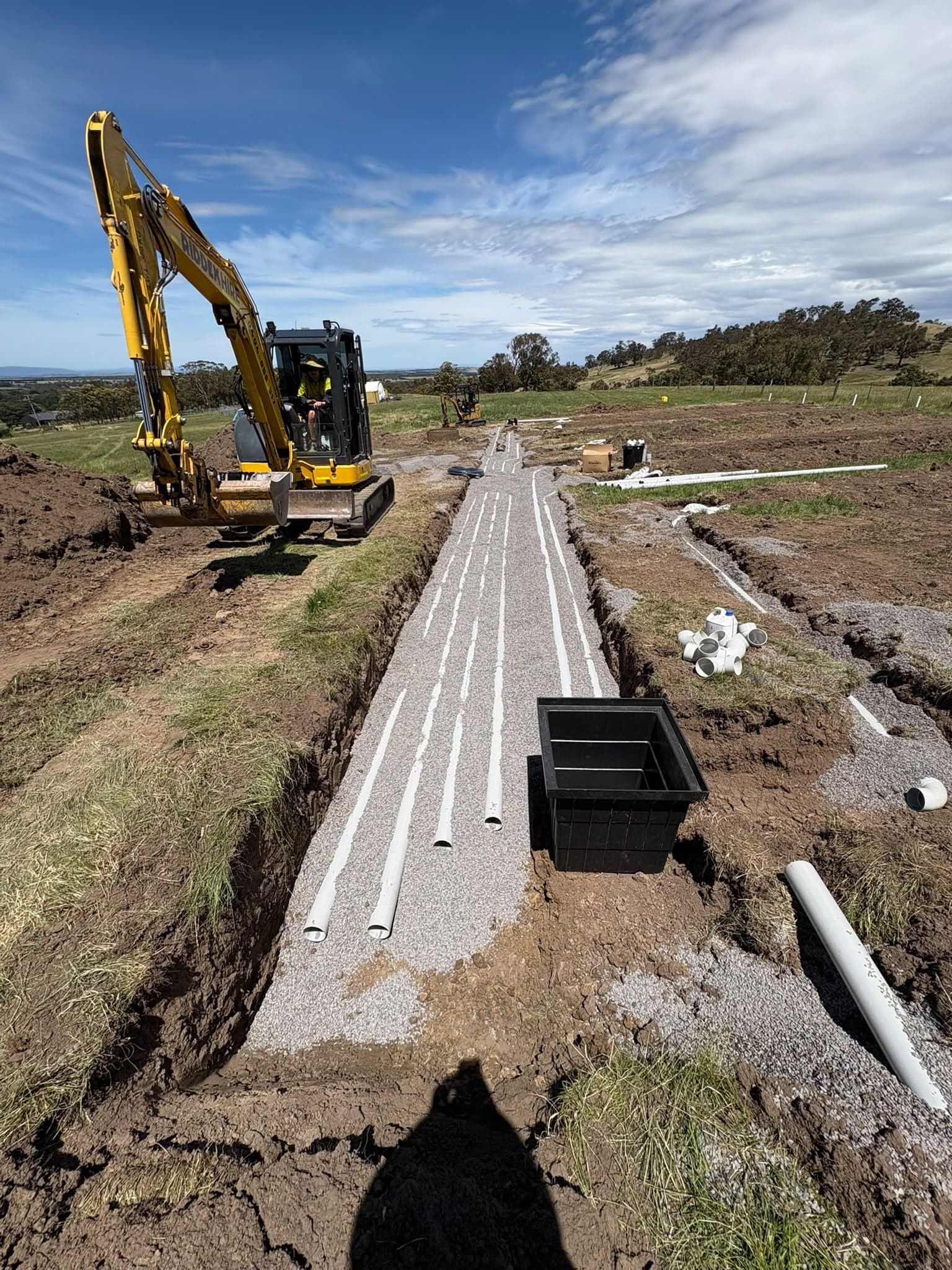 Prava excavator laying new drainage pipes in a trench on a rural site