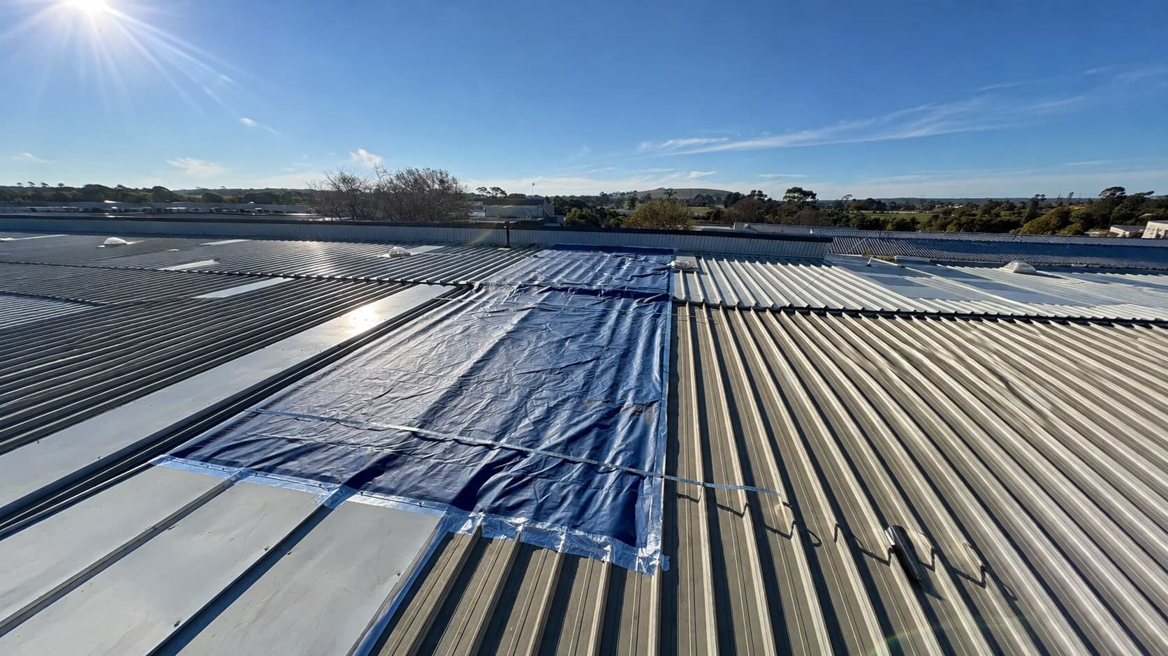 Tarpaulin taped over a damaged section of metal roof as an emergency make-safe