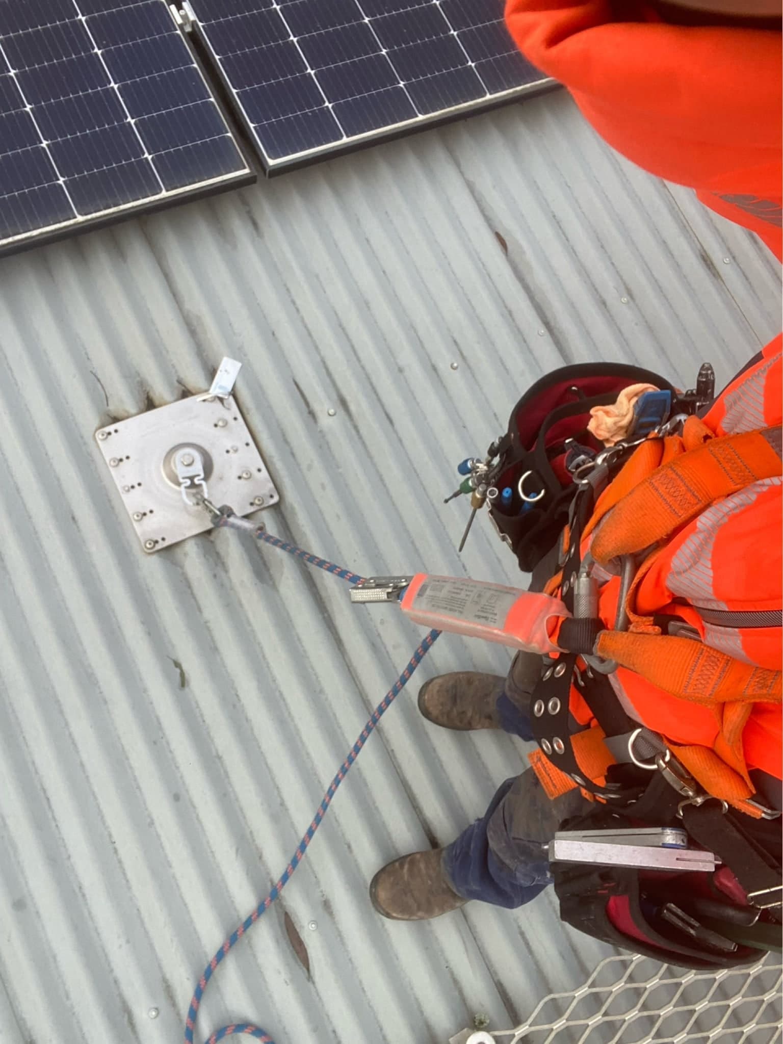 Prava roofer clipped into a roof anchor with a safety harness during a make-safe