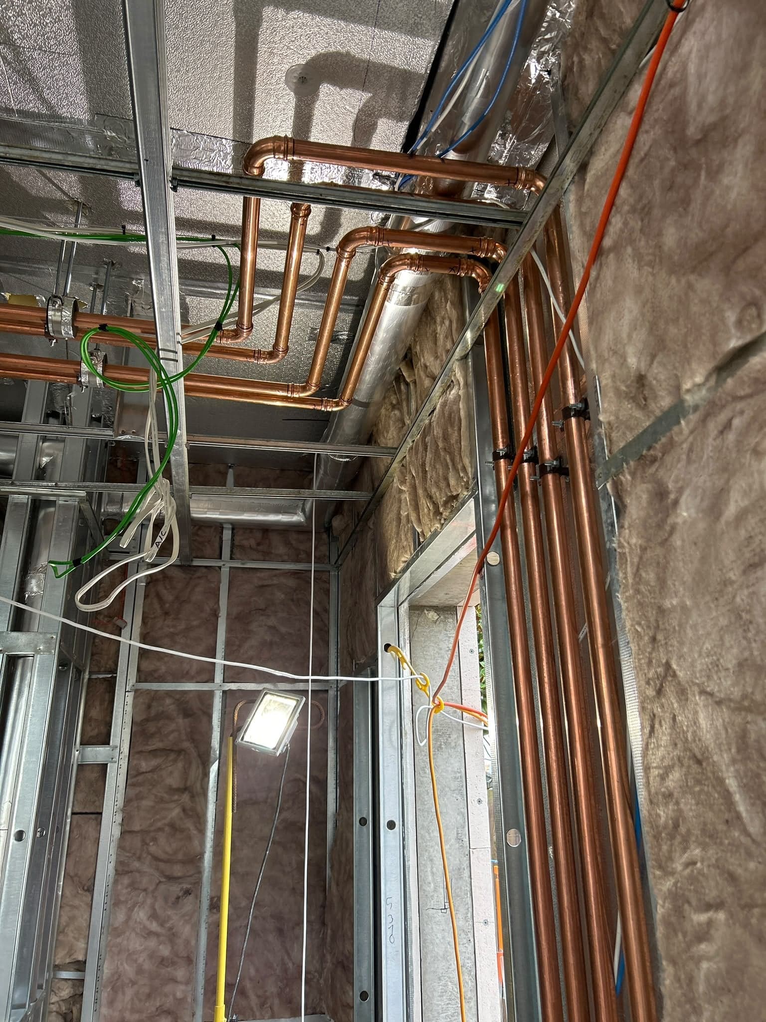 New copper water pipes run through a steel-framed ceiling and wall