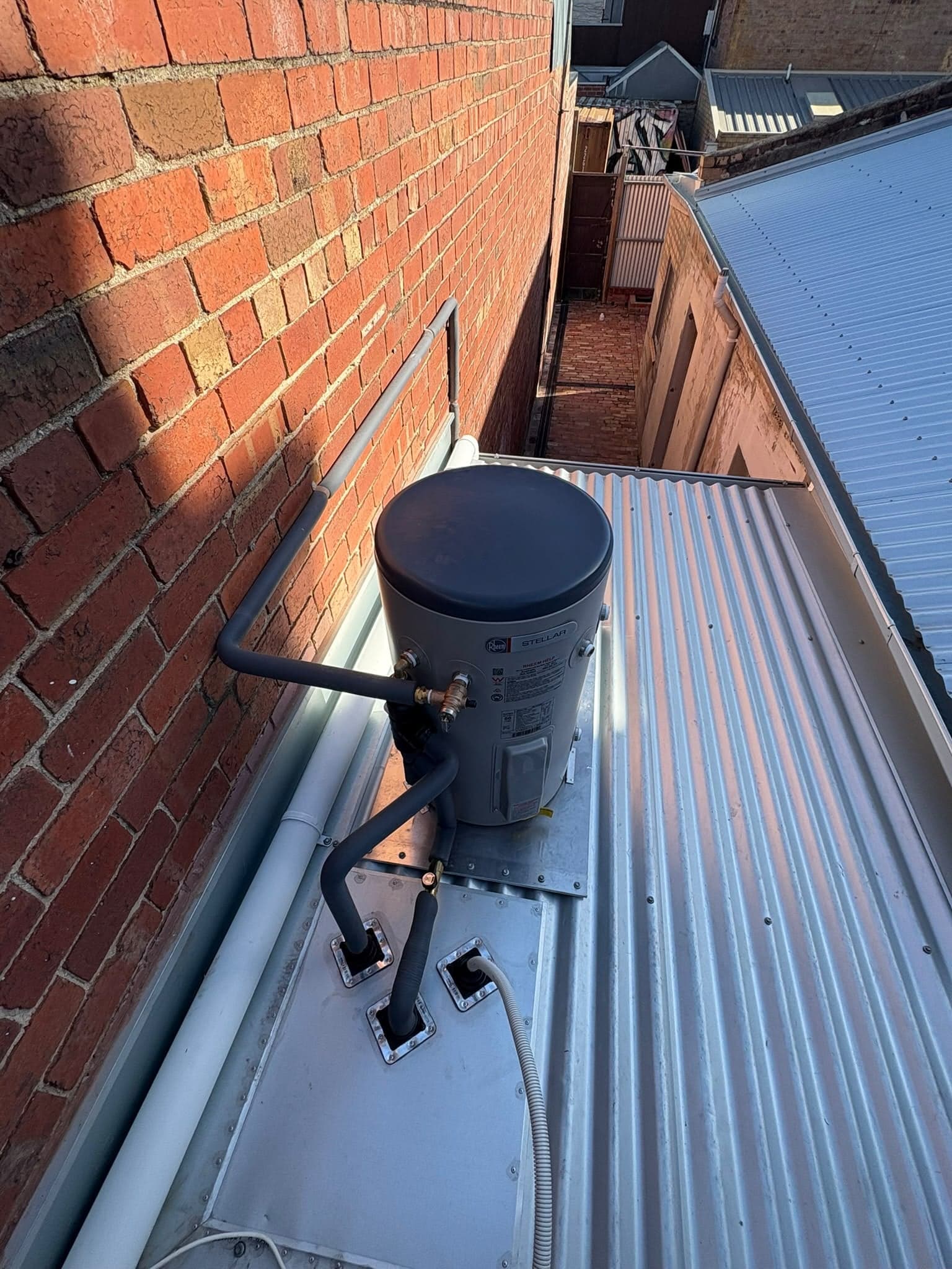 Hot water unit installed on a metal roof beside a brick wall