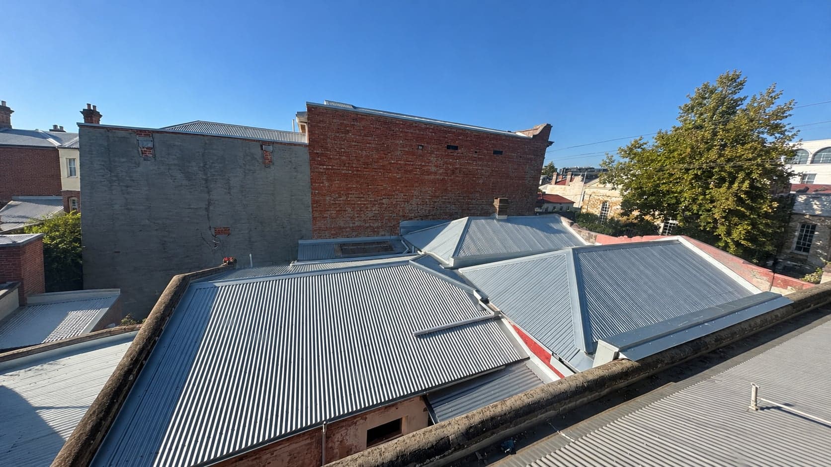 Metal roofs with hips, valleys and gutters beside a brick wall, completed by Prava